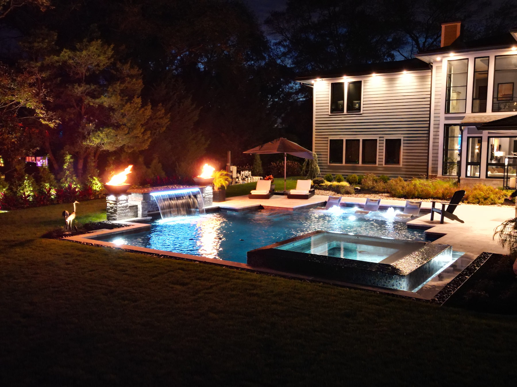Geometric pool with spillover spa, tanning ledge, fire features, waterfall at night